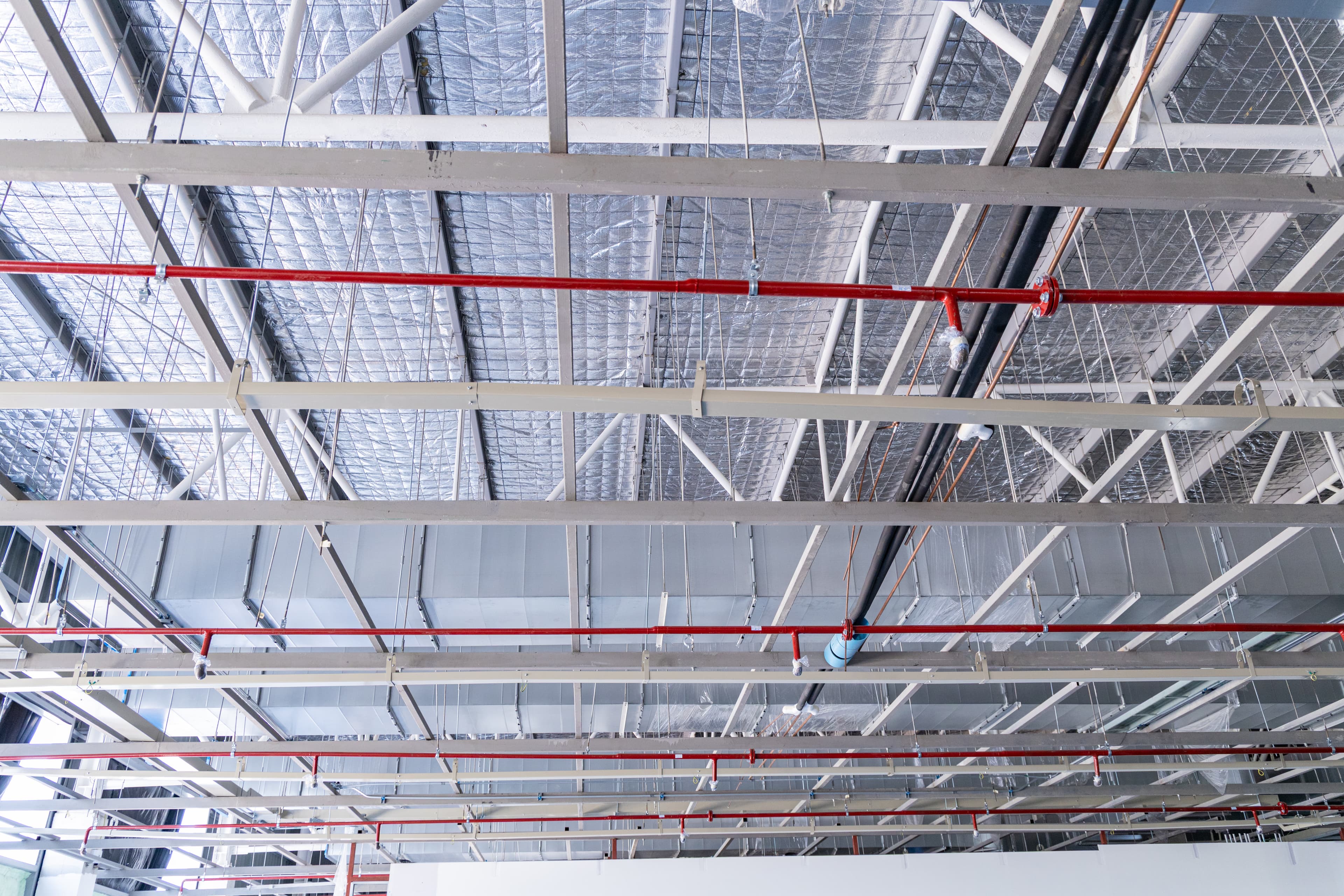 Industrial ceiling with insulated HVAC ducts, red fire sprinkler pipes, and electrical conduit in a commercial building